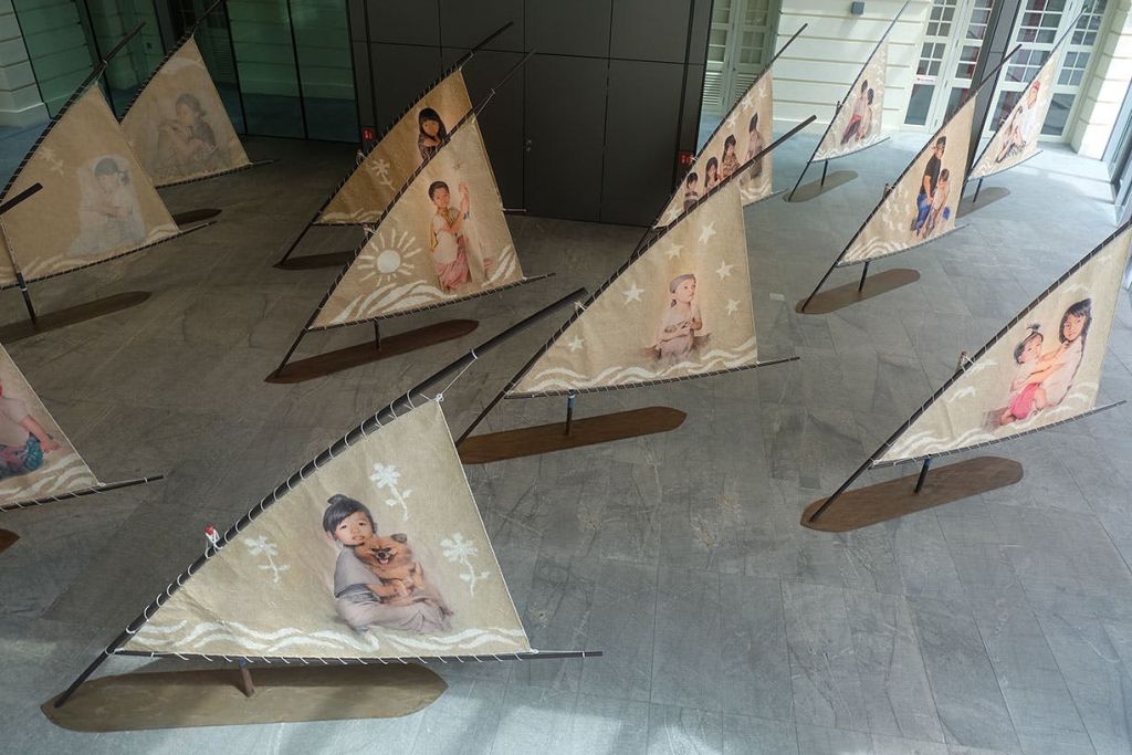 실내에 전시된 여러 개의 삼각형 돛에는 나무 받침대에 장착된 다양한 포즈의 어린이 이미지가 있습니다.