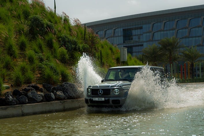 회색 메르세데스-벤츠 SUV가 현대식 건물을 배경으로 측면에 커다란 파도가 넘칩니다.