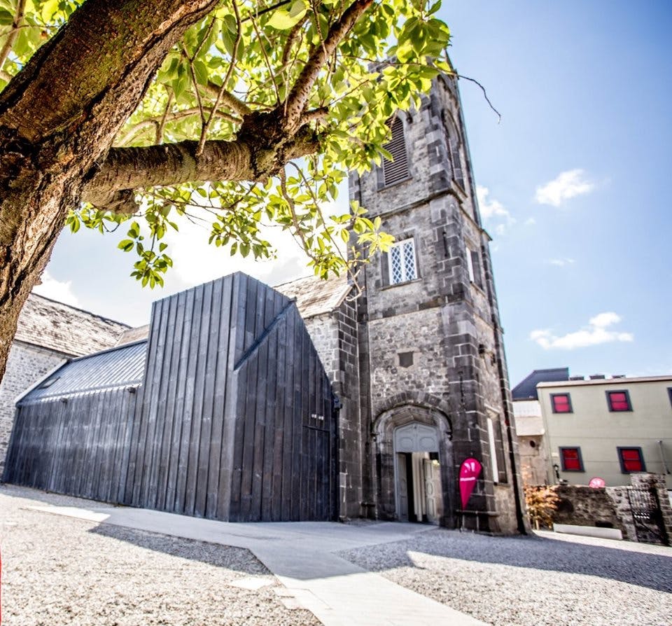 오래된 석탑과 나란히 있는 현대적인 검은색 건물로, 전경에 잎이 무성한 나무가 있고 위에는 맑은 하늘이 있습니다.