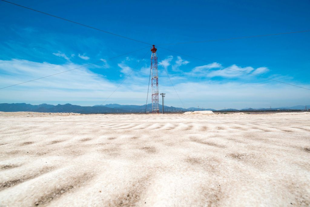 먼 산이 있는 맑고 푸른 하늘 아래 평평하고 하얀 질감의 사막 풍경에 높은 라디오 타워가 서 있습니다.