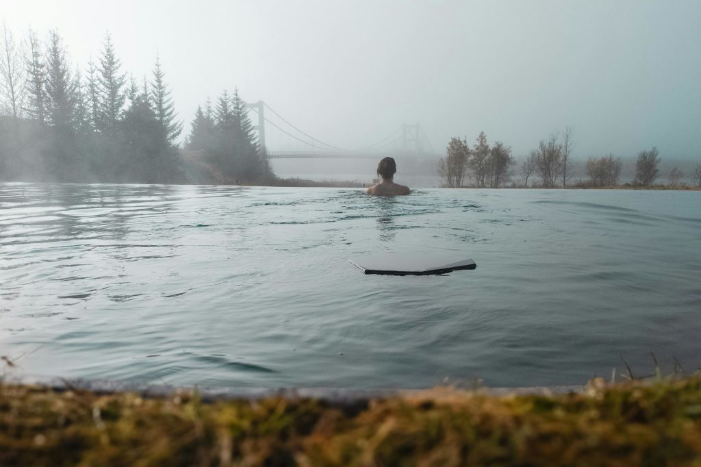 야외 수영장에서 나무와 다리를 배경으로 안개가 자욱한 풍경을 감상하는 사람.