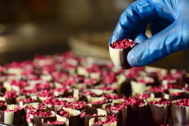 빨간색 토핑이 가득한 작은 디저트를 들고 있는 장갑을 낀 손. 배경에는 비슷한 디저트가 많이 준비되어 있습니다.