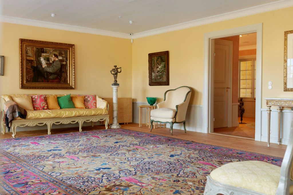 노란색 벽, 무늬 러그, 화려한 색상의 베개가 놓인 소파, 안락의자, 액자에 담긴 예술품이 놓인 아늑한 거실입니다.