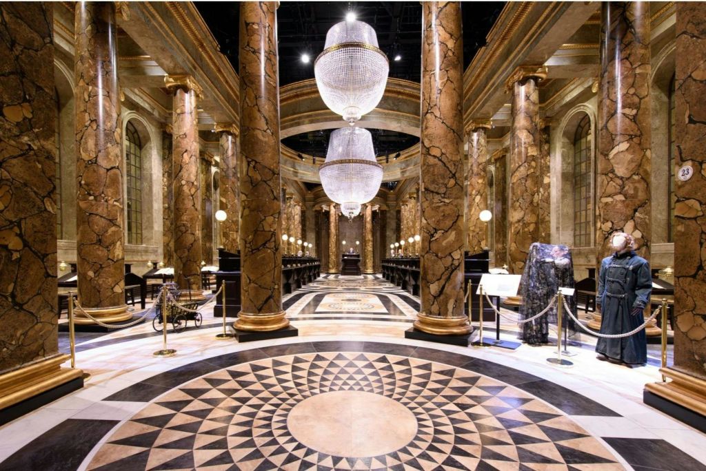 대리석 기둥, 샹들리에, 기하학적 바닥 패턴, 측면을 따라 놓인 책상이 있는 우아한 홀입니다.