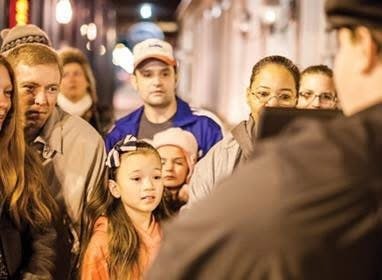 어린이와 성인을 포함한 한 무리의 사람들이 프레임 밖의 무언가를 유심히 바라보며 밤에 야외에 모였습니다.