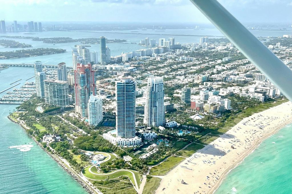 높은 건물, 녹지 공원, 일광욕과 수영을 즐기는 사람들이 있는 모래 해변이 있는 해안 도시의 공중 전망.