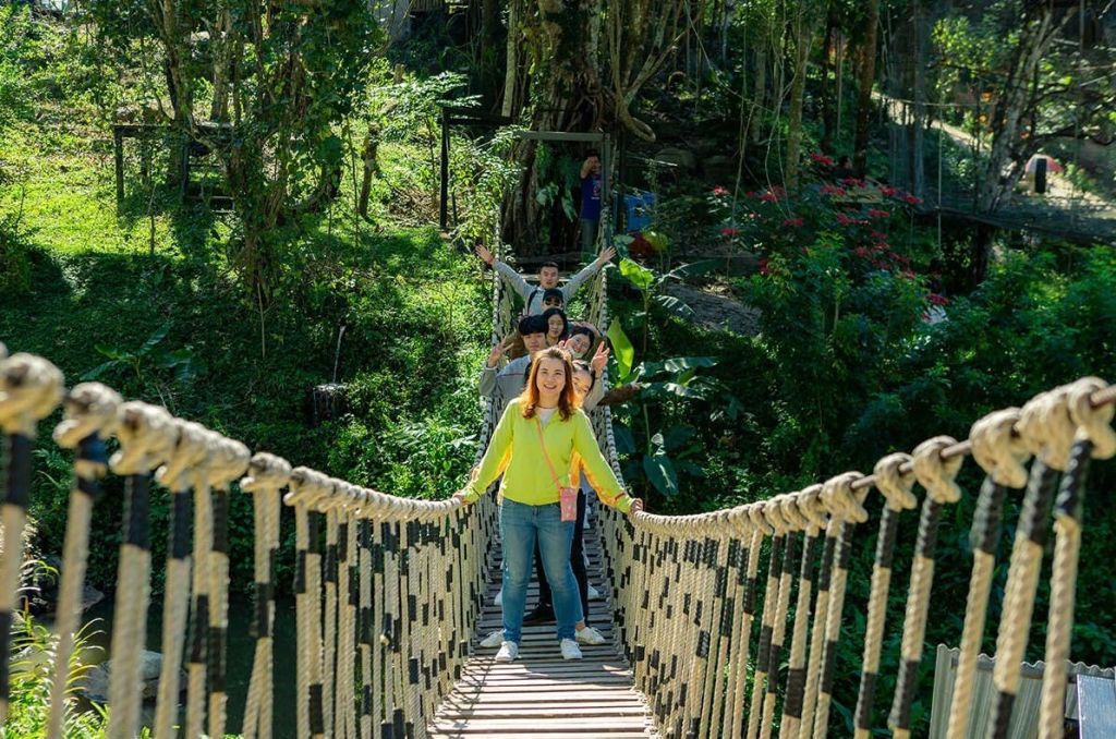 녹음이 우거진 밧줄 다리에 서서 미소를 짓고 카메라를 향해 포즈를 취하는 사람들.