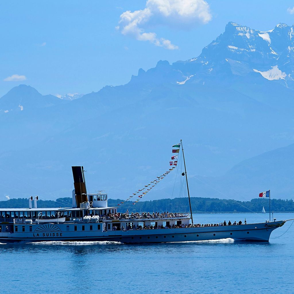 맑고 푸른 하늘 아래 산을 배경으로 잔잔한 호수에서 "라 스위스" 라는 이름의 보트가 항해합니다.