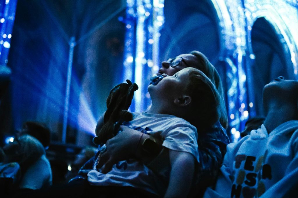 어른과 아이가 위를 바라보며 푸른 빛이 감도는 공간에 함께 앉아 박제된 장난감을 들고 있습니다.