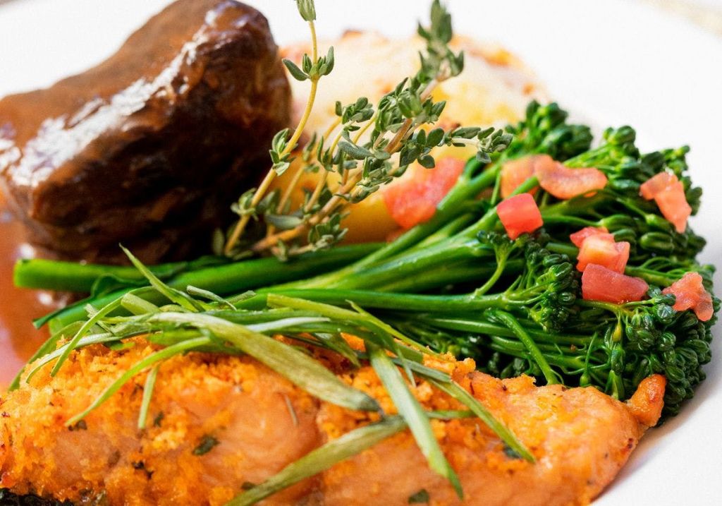 구운 고기, 브로콜리, 잘게 썬 토마토, 허브가 들어간 도금 요리를 클로즈업한 사진입니다.