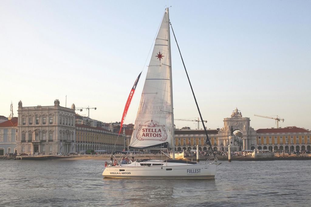 맑은 하늘 아래 역사적인 건물 근처에 있는 만에서 "스텔라 아르투아" 브랜드가 있는 요트.