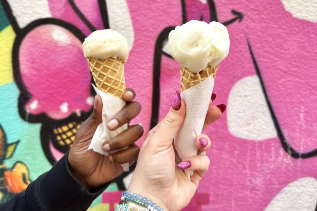그래피티로 덮인 벽 앞에서 아이스크림 콘을 들고 있는 두 명의 여성 손