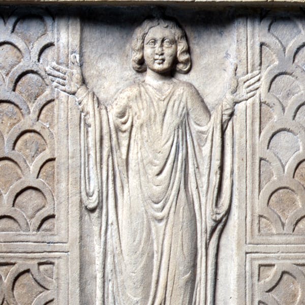 양쪽에 화려한 아치형 패턴이 장식된 드레이프 로브를 착용한 채 양손을 뻗은 인물의 돌 기복.