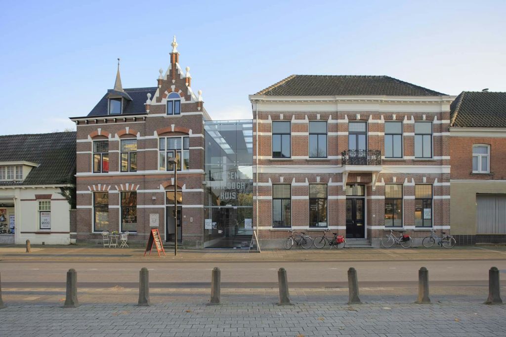 유리 입구가 있는 두 개의 벽돌 건물이 인접해 있습니다. 자전거가 정면에 주차되어 있고, 보도에 의자가 있는 테이블이 있습니다.