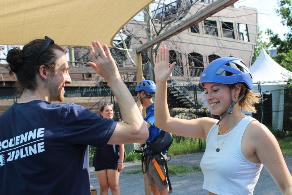 헬멧을 쓴 사람이 웃으며 하이파이브를 하고 있습니다. 배경에 있는 사람들도 비슷한 시설을 갖추고 있습니다. 야외 환경.