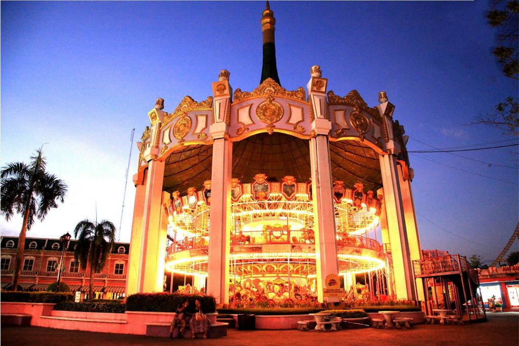 해질 무렵 2층 회전목마에 화려한 황금 장식과 근처에 앉아 있는 몇 명의 사람들이 조명을 비췄습니다.