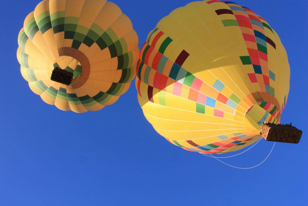 패치워크 디자인의 두 개의 다채로운 열기구가 맑고 푸른 하늘을 배경으로 솟아 있습니다.