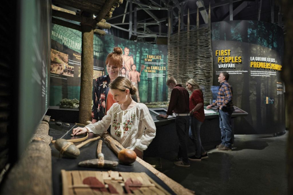 한 여성과 어린이가 박물관에서 선사 시대 전시를 관람하고 있습니다. 다른 방문자가 백그라운드에서 디스플레이를 보고 있습니다.