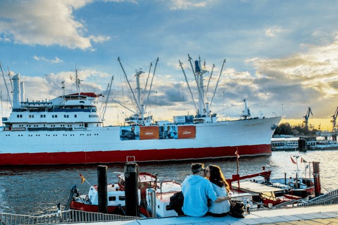 부두에 앉아 부분적으로 흐린 하늘 아래에서 흰색과 빨간색의 커다란 배를 껴안고 마주보고 있습니다.