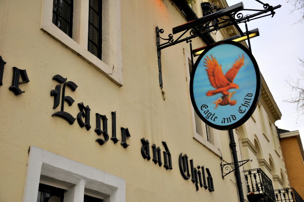 베이지색 건물 외벽에 설치된 아이를 태운 독수리와 함께 "Eagle and Child" 펍에 서명하세요.