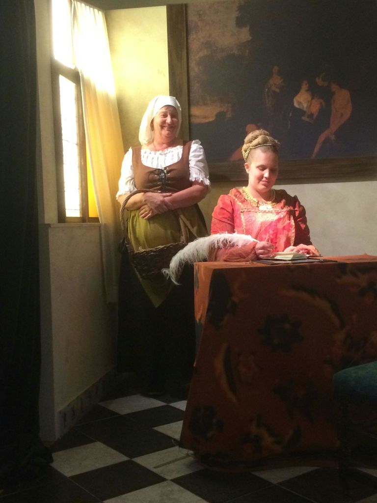 희미한 조명이 켜진 방 안에 마침표를 찍은 두 명의 여성이 앉아 깃털로 쓰여진 테이블에 앉았고, 다른 한 여성은 웃으며 서 있었습니다.