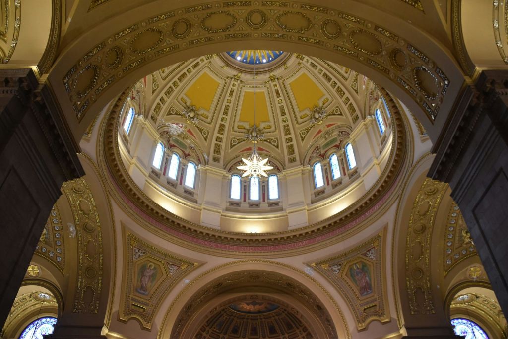 디테일한 금장 장식, 아치형 창문, 중앙 샹들리에가 있는 건물의 화려한 내부 돔입니다.