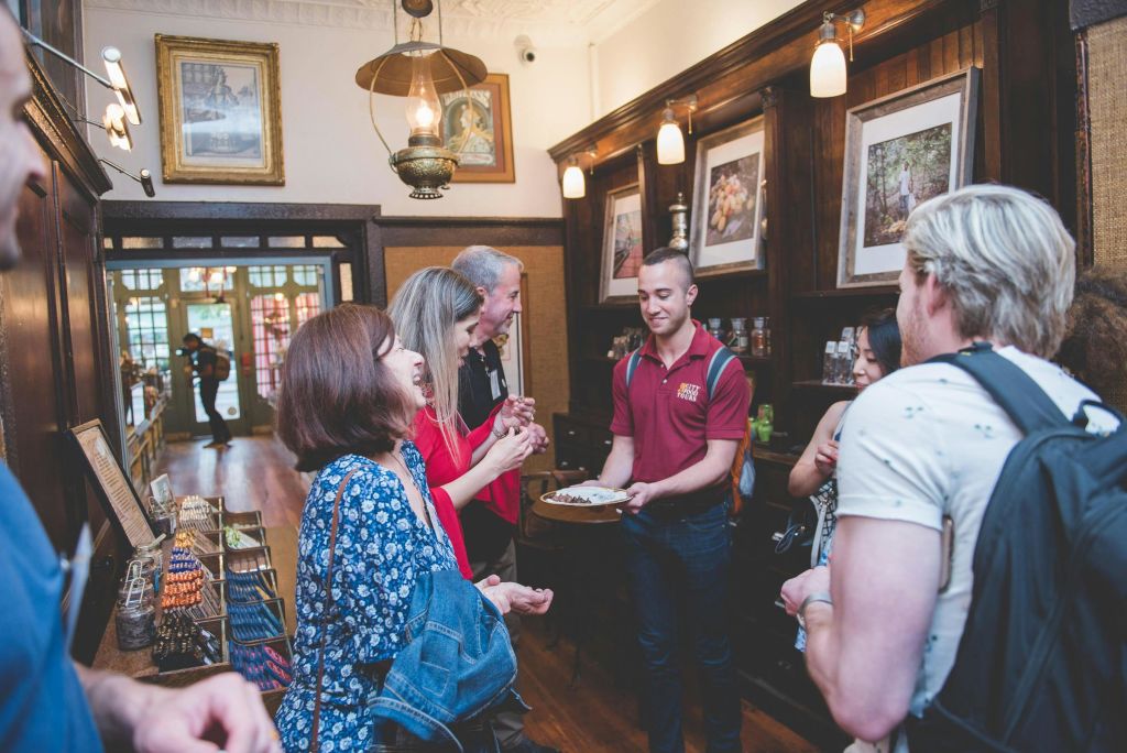따뜻한 나무 장식으로 둘러싸인 음식 쟁반을 들고 있는 한 남성과 상호 작용하는 아늑한 실내 환경에 있는 한 무리의 사람들.