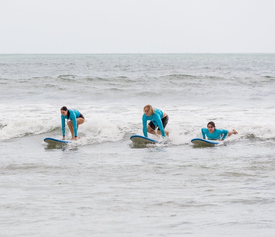 푸른 잠수복을 입은 세 사람이 바다의 푸른 서핑 보드에서 작은 파도를 타고 서핑을 하고 있습니다.