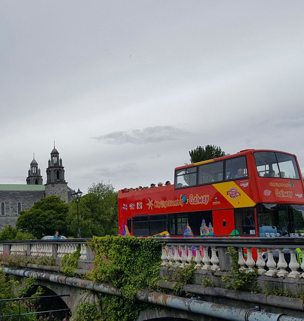 탑을 배경으로 오래된 석조 건물이 있는 다리를 건너는 빨간색 2층 투어 버스가 있습니다.