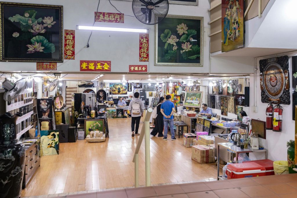 벽에 그림과 장식이 있고, 고객들이 둘러보고, 예술가들이 테이블에서 작업하는 아트숍입니다.