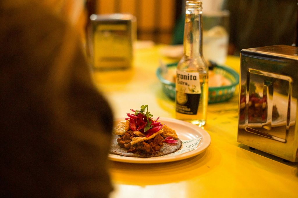 장식이 있는 음식 접시와 노란색 테이블 위에 놓인 맥주 한 병, 다른 물품과 흐릿한 배경이 보입니다.