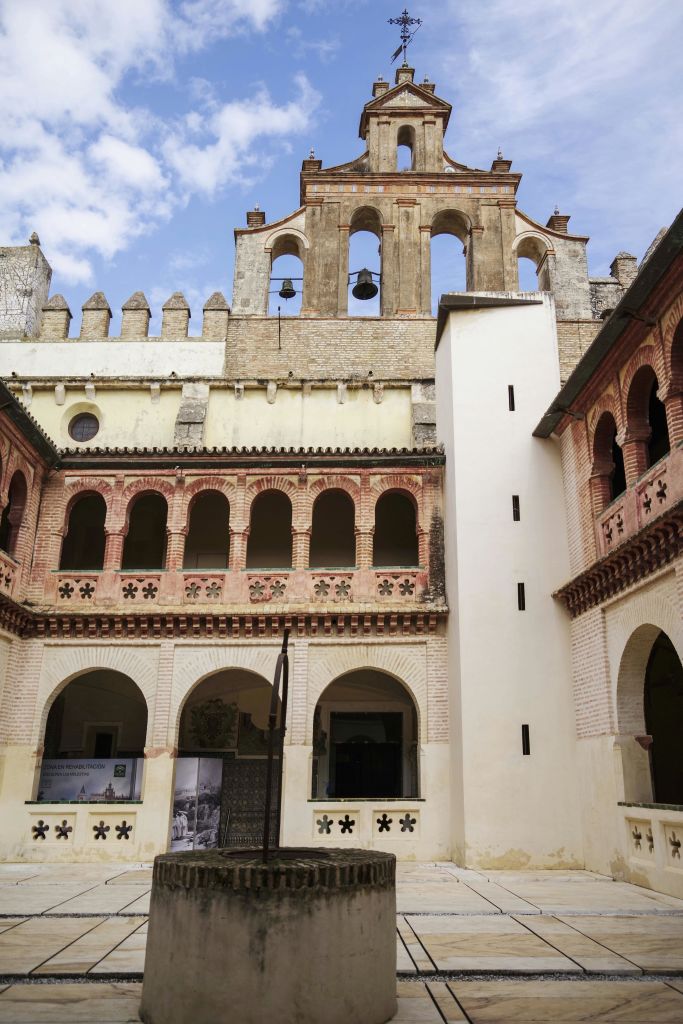 아치형 창문, 벽돌 벽, 부분적으로 흐린 하늘 아래 종탑이 있는 유서 깊은 안뜰.