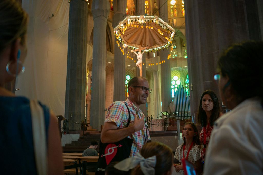 화려한 스테인드글라스 창문과 머리 위로 커다랗고 화려한 샹들리에가 있는 대성당 안에 한 무리의 사람들이 있습니다.