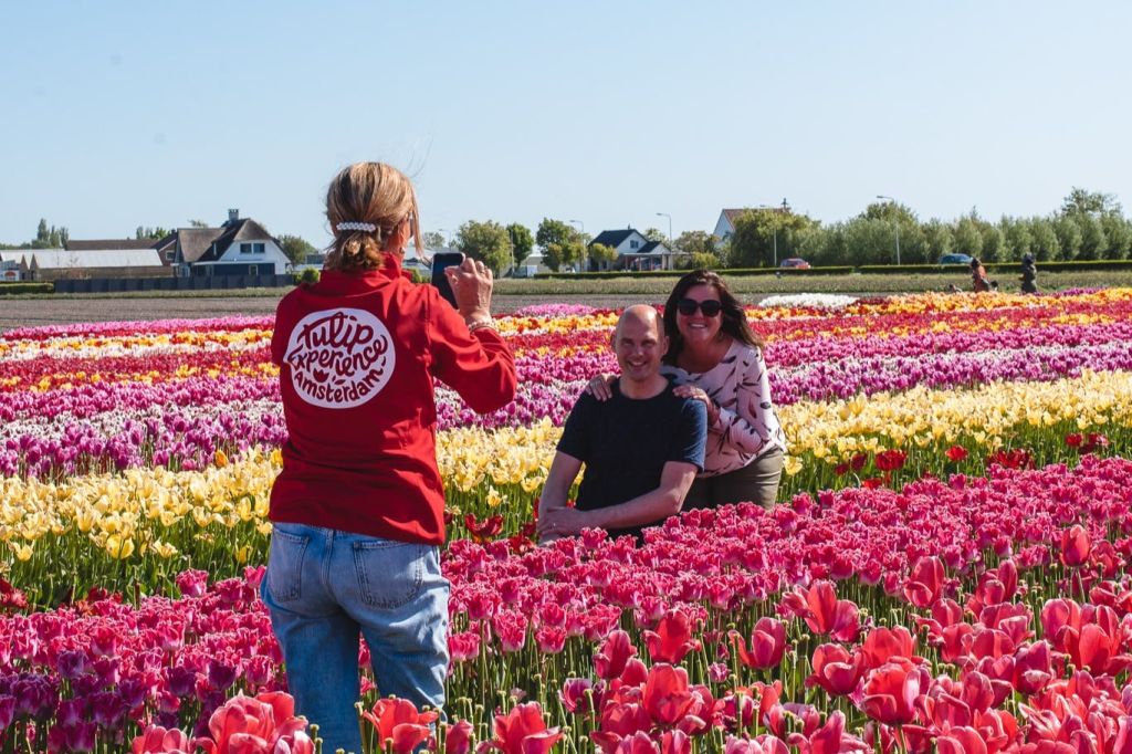 화창한 날씨에 집과 나무를 배경으로 화려한 튤립밭에서 포즈를 취하고 있는 커플의 모습을 촬영한 사진입니다.
