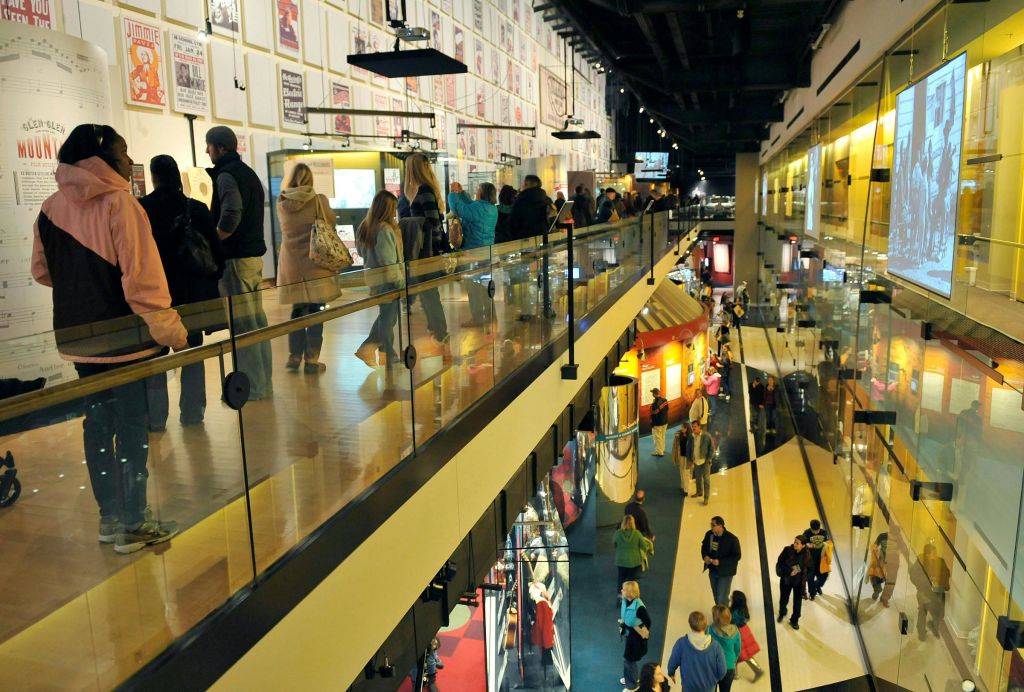 벽에 유리 난간, 여러 개의 디스플레이, 액자에 담긴 포스터가 놓인 2층 내부 공간을 따라 사람들이 거닐고 있습니다.