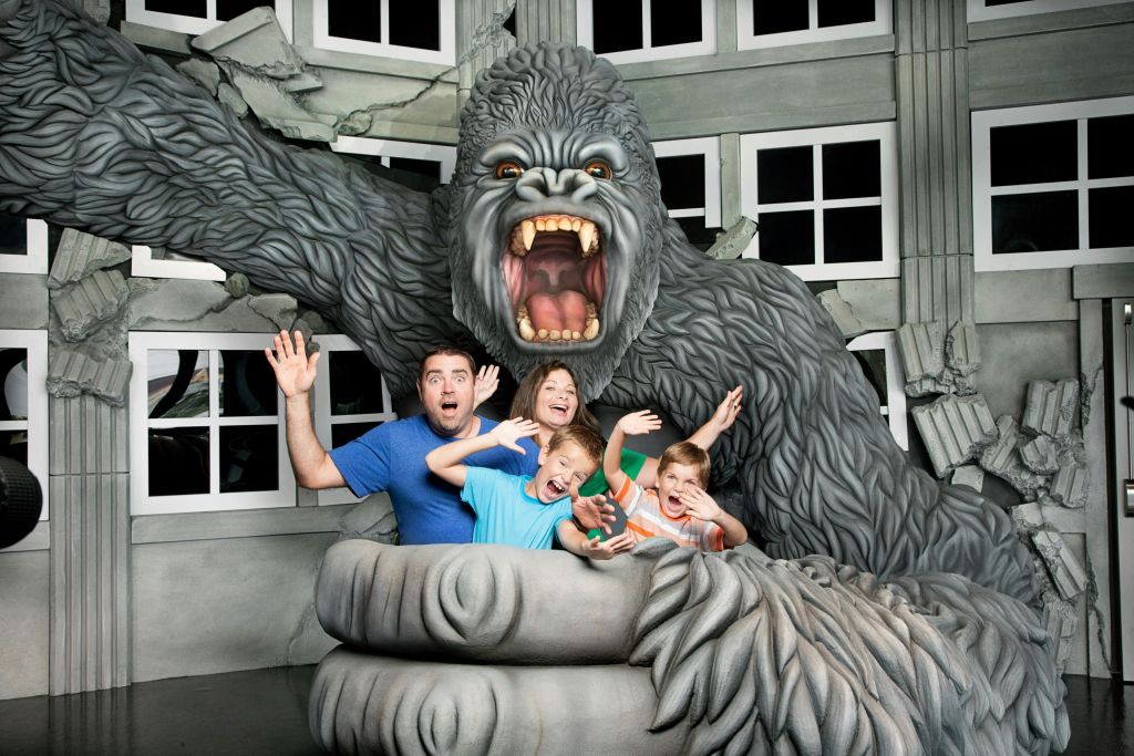 유인원의 입을 활짝 벌린 채 커다란 킹콩 조각상 품 안에서 신나는 포즈를 취하고 있는 가족.