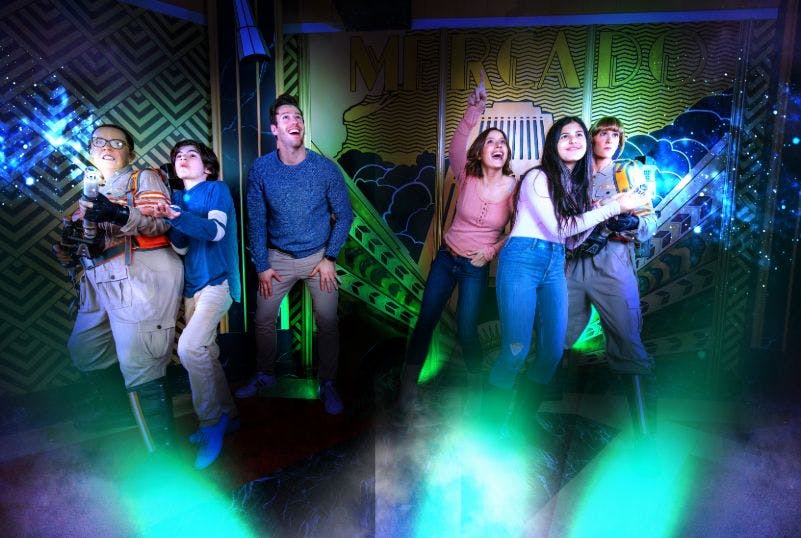 캐주얼 의류를 입은 4명의 사람들이 화려한 조명과 거울을 배경으로 빛에 기반한 인터랙티브 전시회에 참여하고 있습니다.