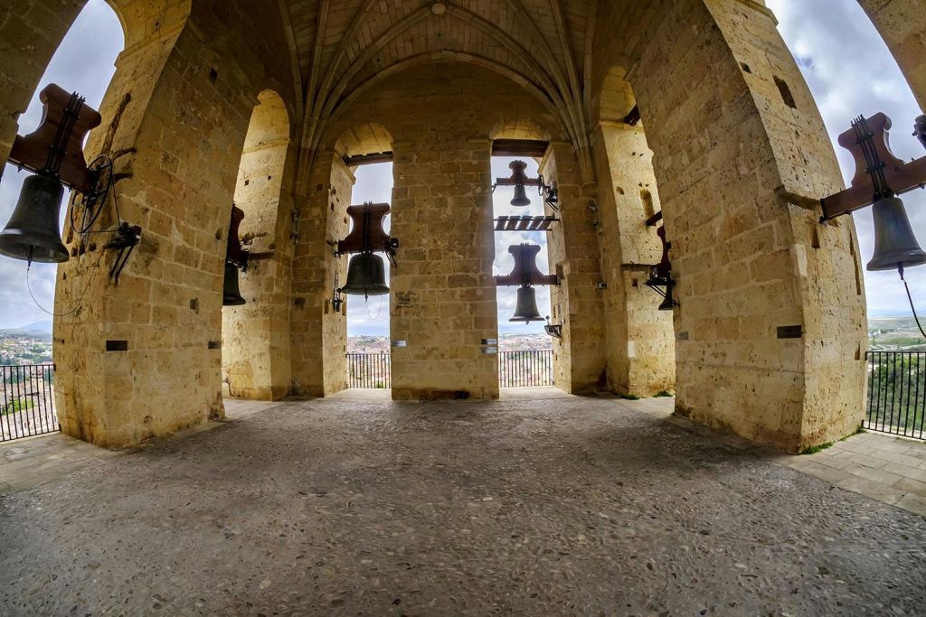 아치형 통로에 여러 개의 커다란 종을 매달아 놓은 석조 종탑의 내부 모습. 개구부를 통해 도시 풍경이 보입니다.