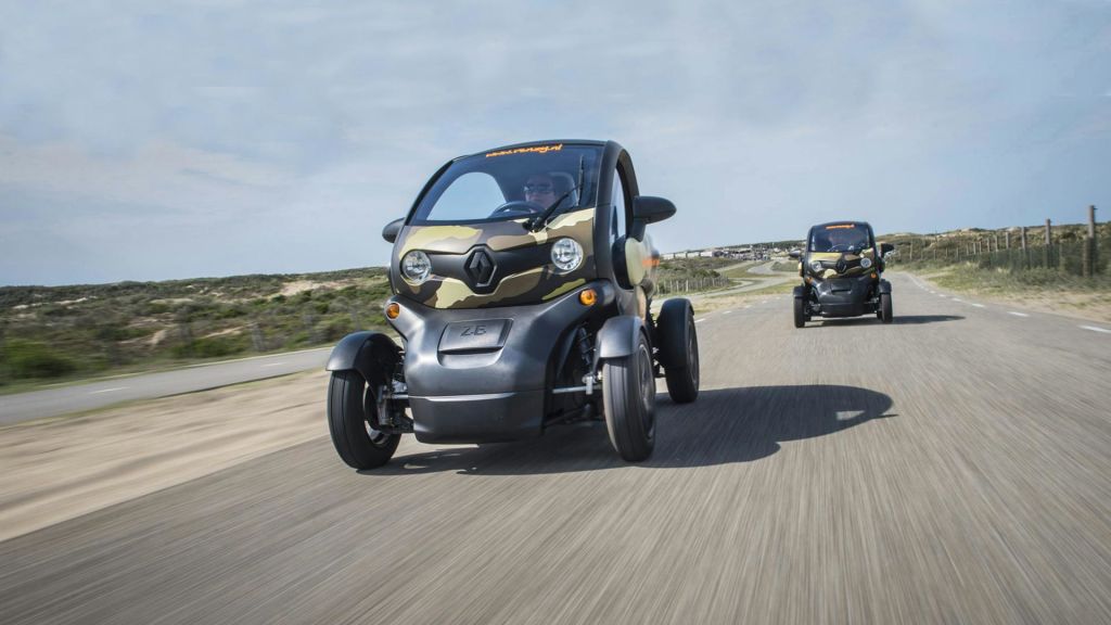 풍경을 배경으로 도로를 달리는 위장된 소형 전기차 2대.