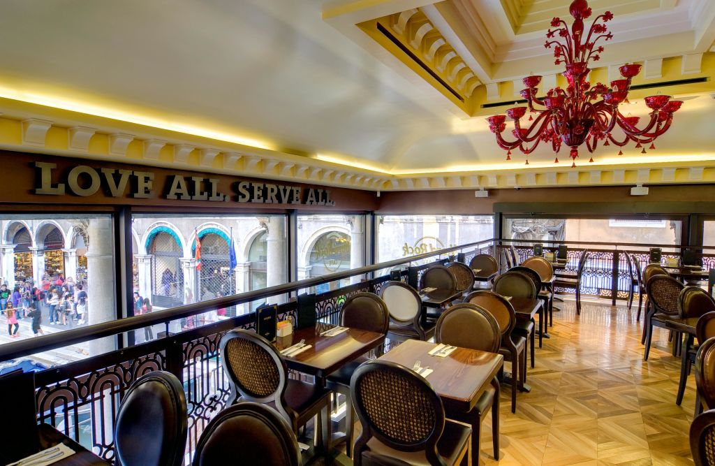 갈색 의자, 나무 테이블, 빨간 샹들리에, 건축학적 거리 전망이 내려다보이는 커다란 창문이 있는 현대적인 실내 식사 공간.