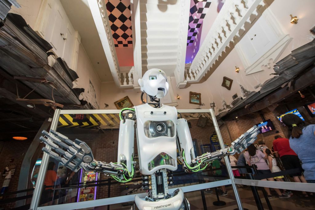 노출형 메커니즘을 갖춘 휴머노이드 로봇이 기울어진 액자와 체크무늬 천장이 있는 기발하고 박물관 같은 공간에 서 있습니다.