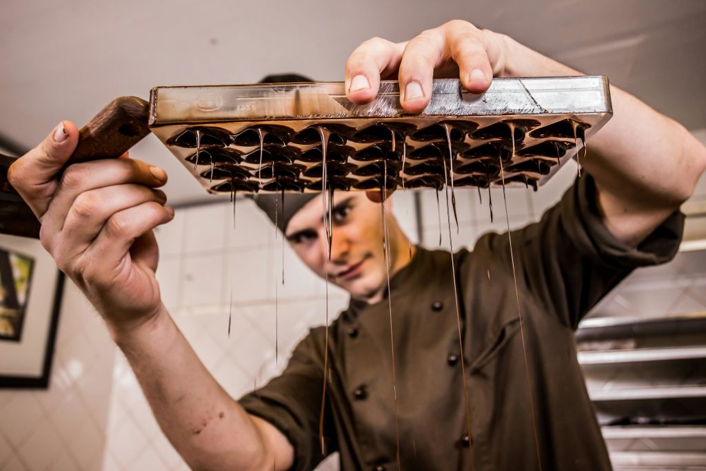 셰프의 유니폼을 입은 사람이 녹은 초콜릿이 떨어지는 초콜릿 틀을 거꾸로 들고 있습니다.