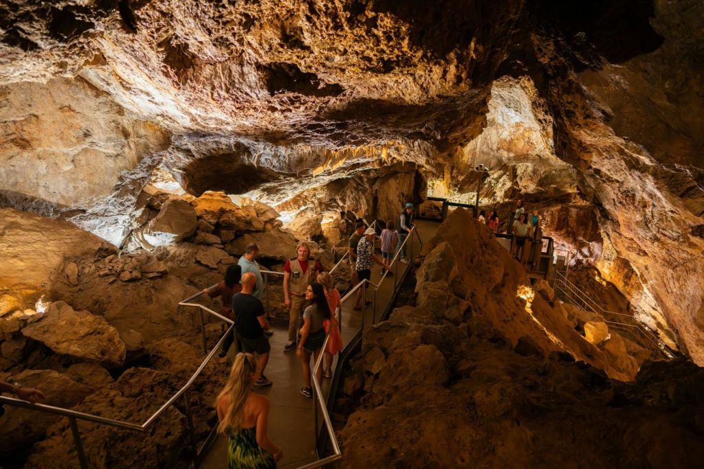 암석 지층이 있는 어두운 동굴을 탐험하고 난간이 있는 지정된 길을 걷는 사람들.