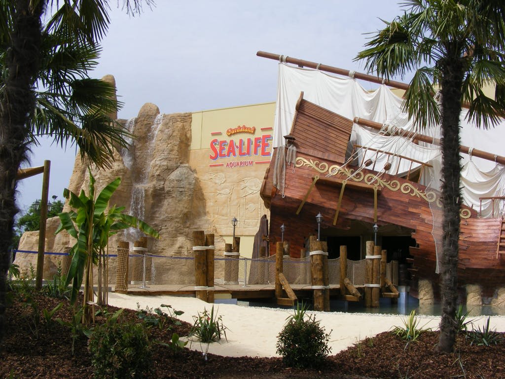 열대 식물로 둘러싸인 시 라이프 수족관 입구의 바위 벽에 부착된 해적선 구조물입니다.