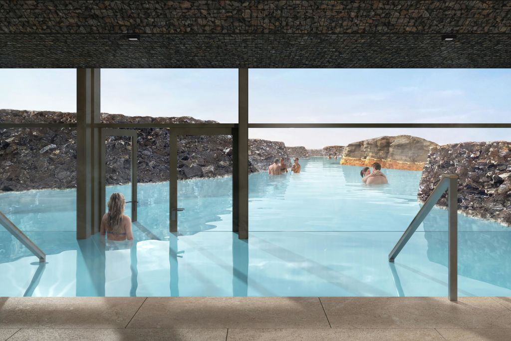 바위 지형으로 둘러싸인 지열 수영장에서 휴식을 취하는 사람들로, 실내에서 커다란 유리창을 통해 볼 수 있습니다.