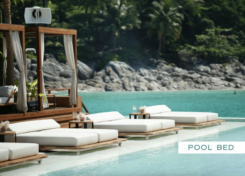 청록색 수영장 옆의 흰색 선베드와 작은 테이블이 있는 라운지 공간으로, 바위와 울창한 녹지를 배경으로 꾸며져 있습니다.