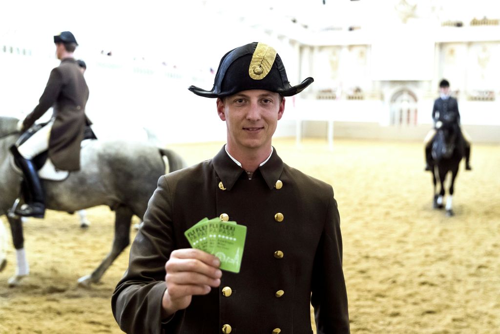 전통적인 유니폼을 입은 남성은 그린 카드를 들고 있으며, 다른 유니폼을 입은 남성은 실내 경기장에서 백마를 타고 있습니다.