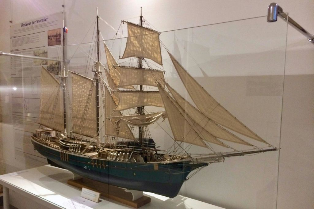 흰색 바탕에 있는 박물관에 전시된 여러 개의 돛대와 돛을 가진 항해 선박의 상세한 모델입니다.