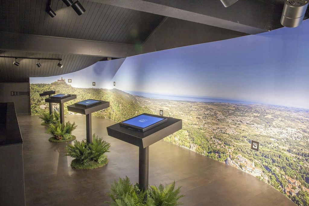 벽에 파노라마 풍경 벽화가 있고 바닥에 장식 식물이 있는 스탠드에는 디지털 스크린이 있는 전시실이 있습니다.