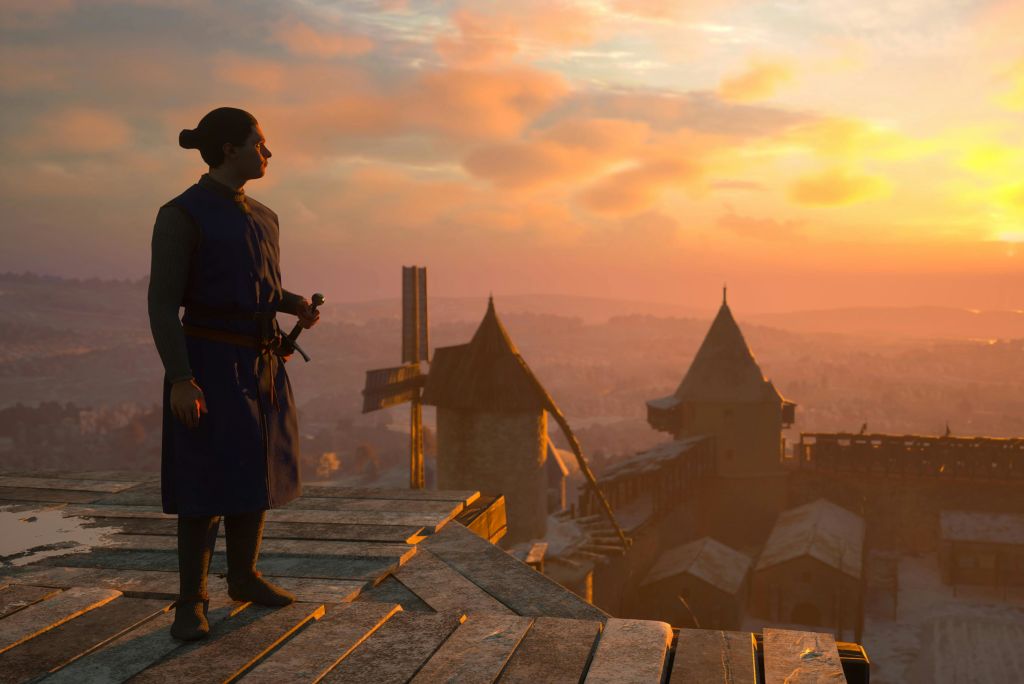 중세 복장을 한 한 사람이 나무 판자 위에 서서 석양이 질 무렵 원뿔 지붕이 있는 성을 내려다보고 있습니다.